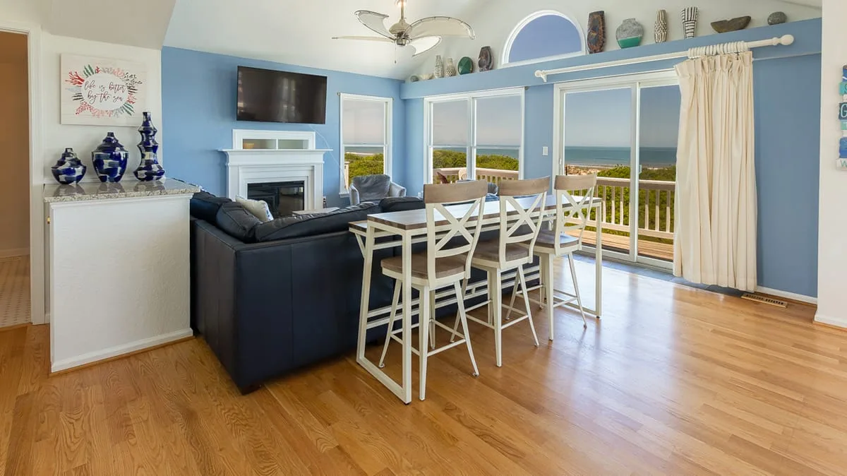 A bright living and dining area with a table, seating, and large windows.