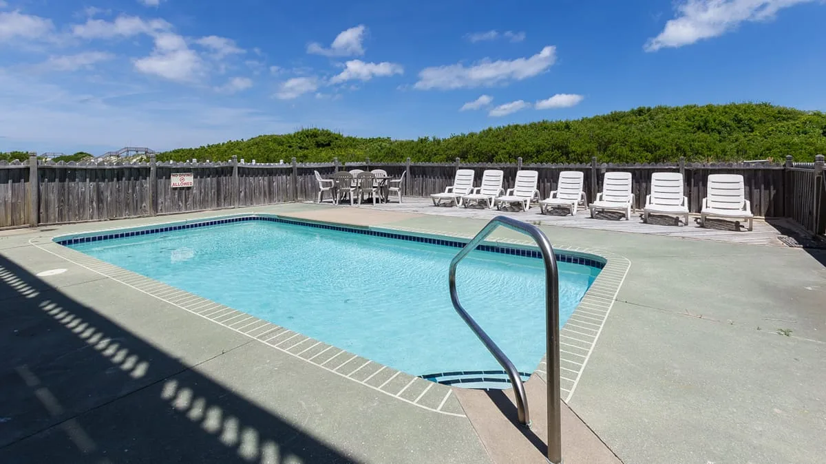 An outdoor swimming pool is surrounded by a paved deck and lounge seating.