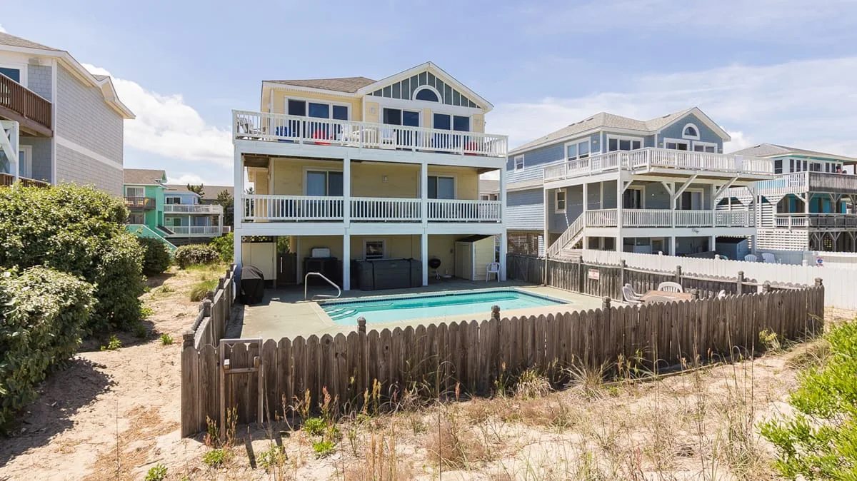 A coastal residential building with balconies overlooks a fenced outdoor pool.