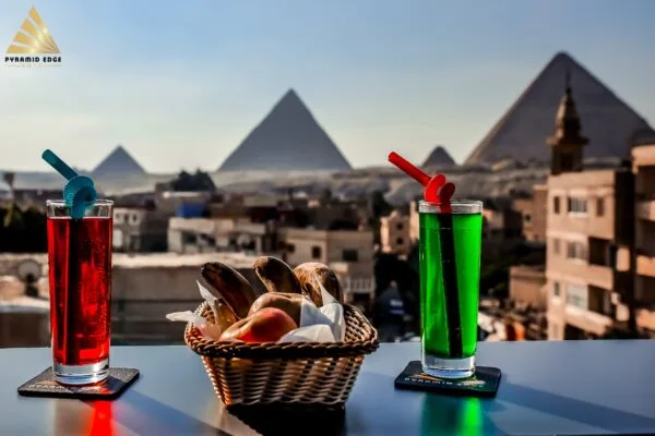 Representative hotel space: Rooftop table with colorful drinks and a basket of snacks, overlooking the pyramids.