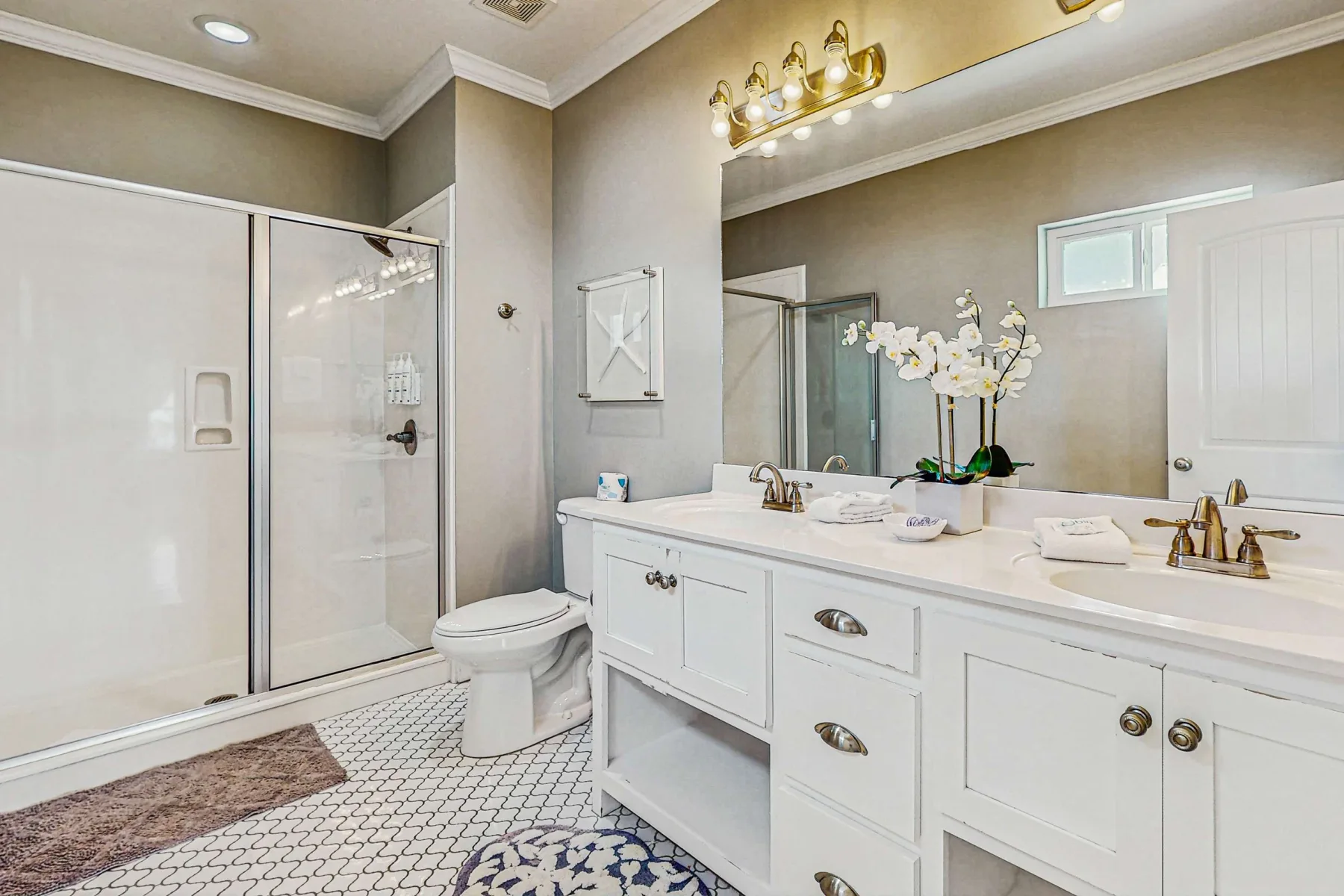 A bright bathroom with a long vanity, large mirror, and glass shower.