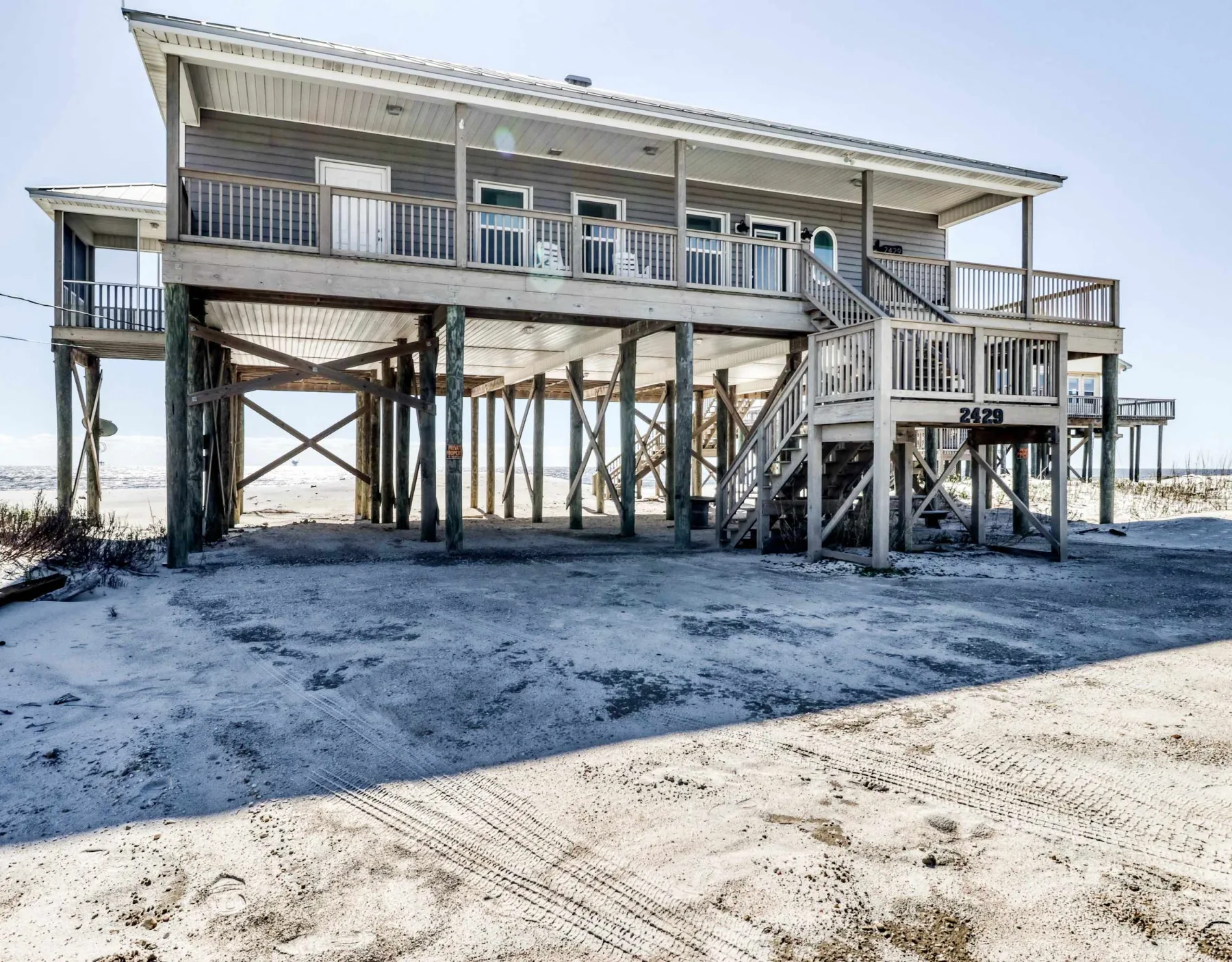 A raised beach house stands on wooden supports above the sandy shore.