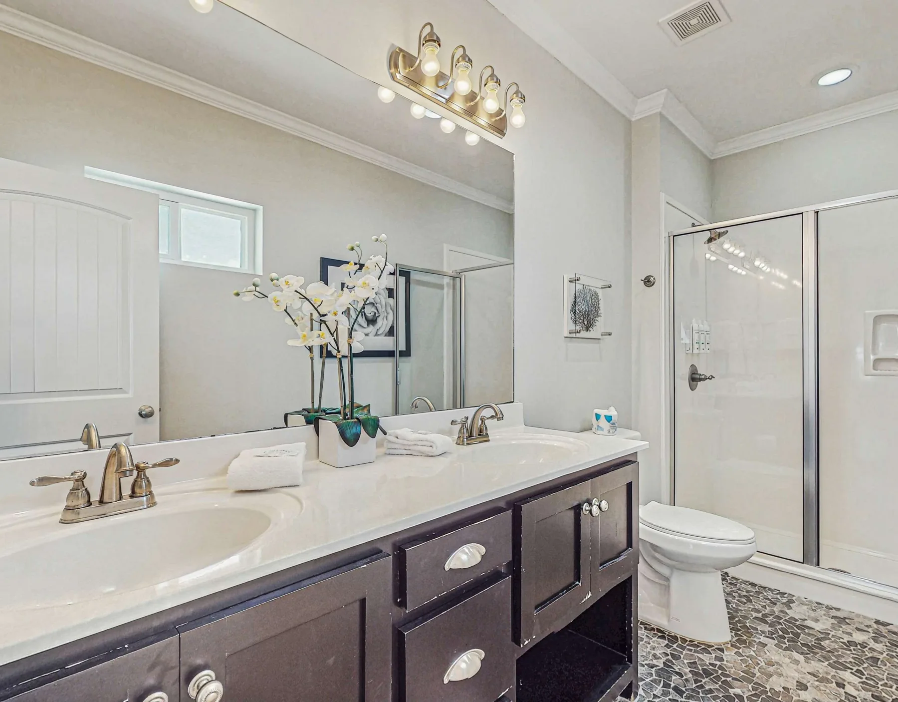 A bright bathroom with a long vanity, wall mirror, and glass shower.