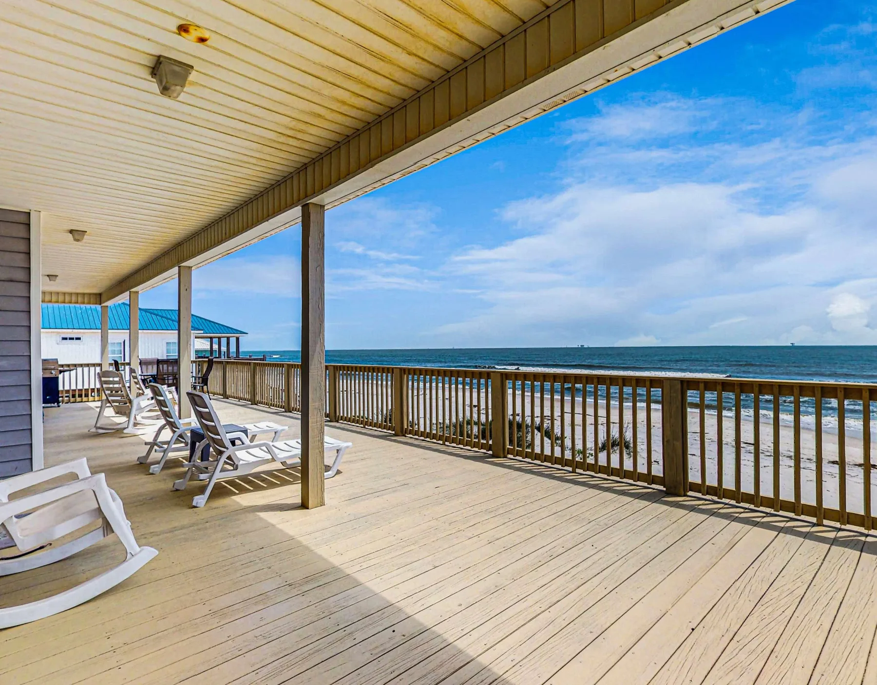 A seaside deck with seating overlooks the ocean beneath a bright blue sky.