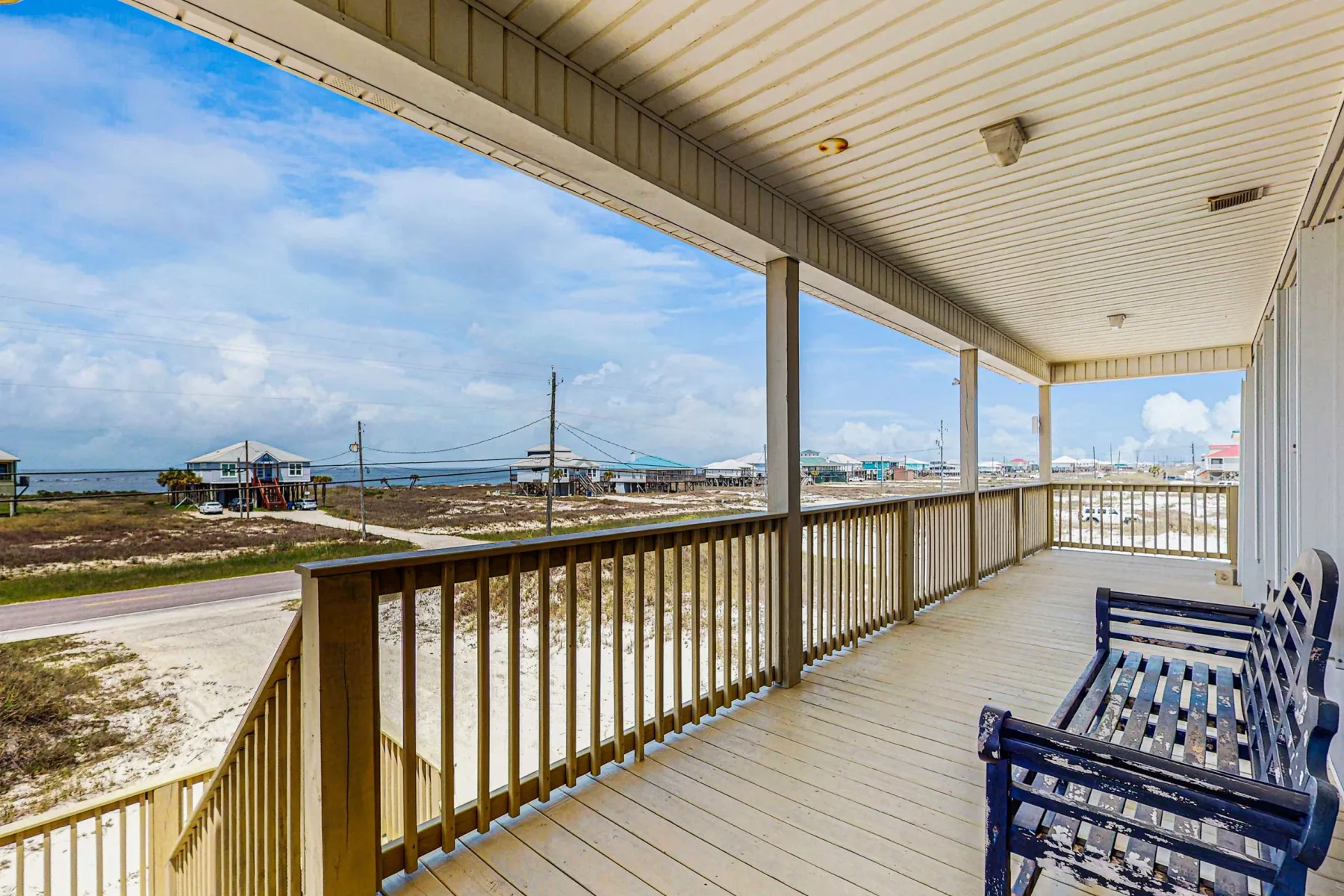 A covered wooden porch overlooks a coastal landscape, with blue seating along the railing.