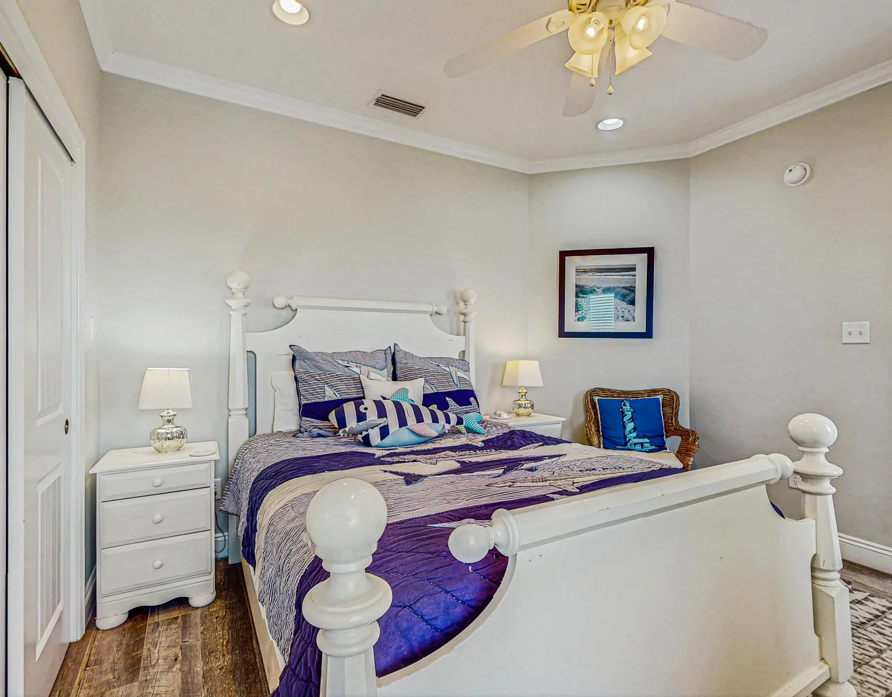 A bedroom with a white bed dressed in purple bedding and a small armchair.