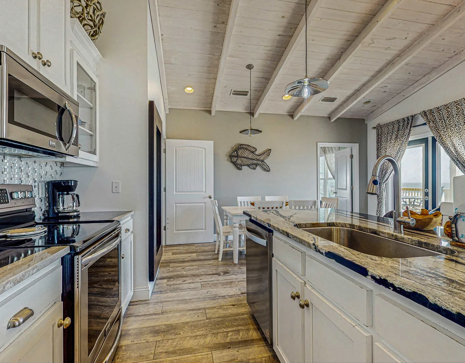 A bright kitchen with a long island, sink, and dining table.