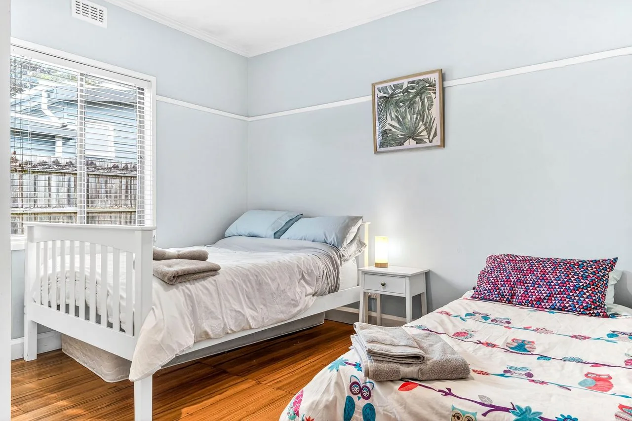 A bright bedroom with two beds, a window, and framed botanical artwork.