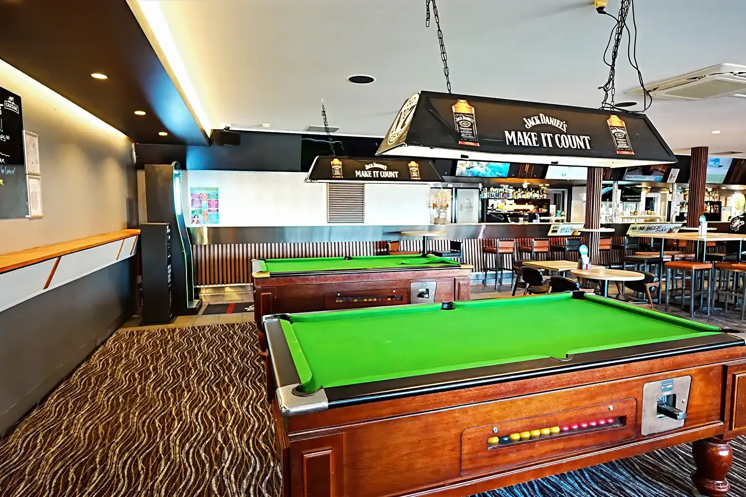 Espacio representativo del hotel: Una mesa de billar ocupa el primer plano de un bar y comedor bien iluminado.