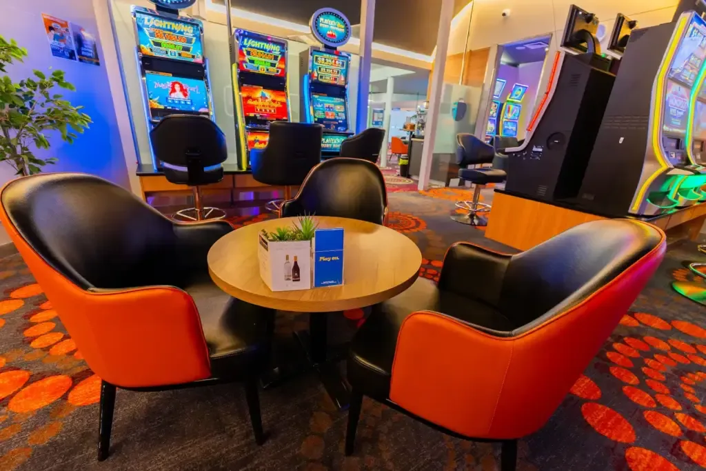 Espacio representativo del hotel: Zona de juegos de casino con máquinas tragamonedas y asientos alrededor de una mesa.