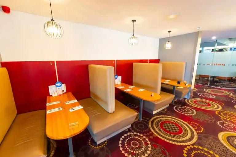 Espacio representativo del hotel: Un comedor con asientos tipo cabina y mesas junto a una mampara de vidrio.