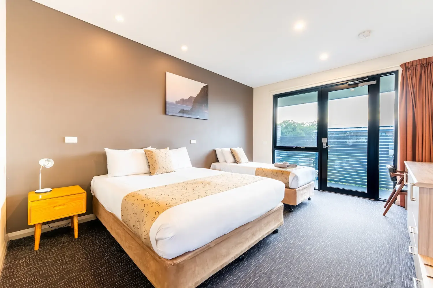 Espacio representativo del hotel: Dormitorio con dos camas, una mesita de noche y puertas de vidrio que dan a un balcón.