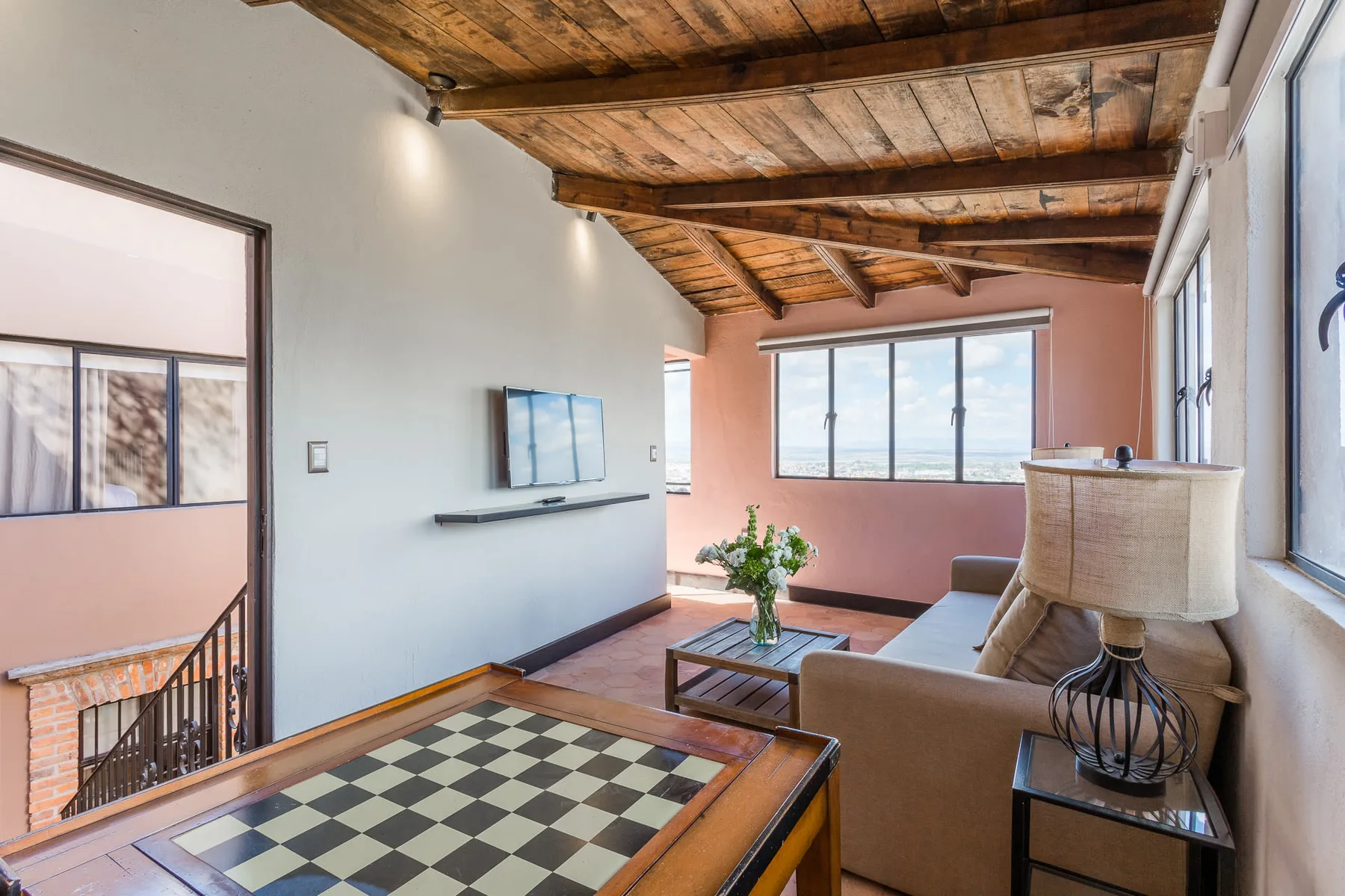 A living room with seating, a coffee table, and large windows beneath exposed wooden beams.