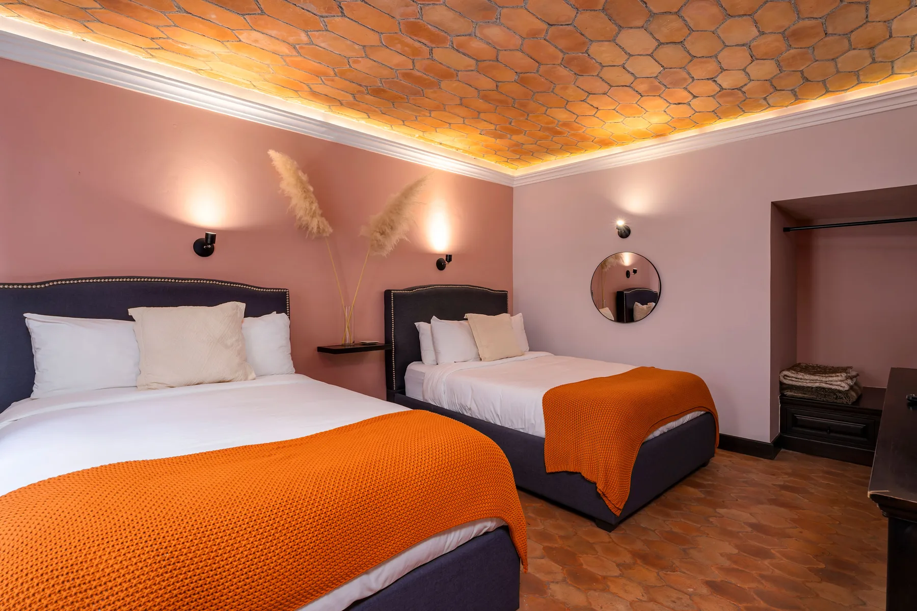 A bedroom with two beds, orange blankets, and a patterned ceiling.