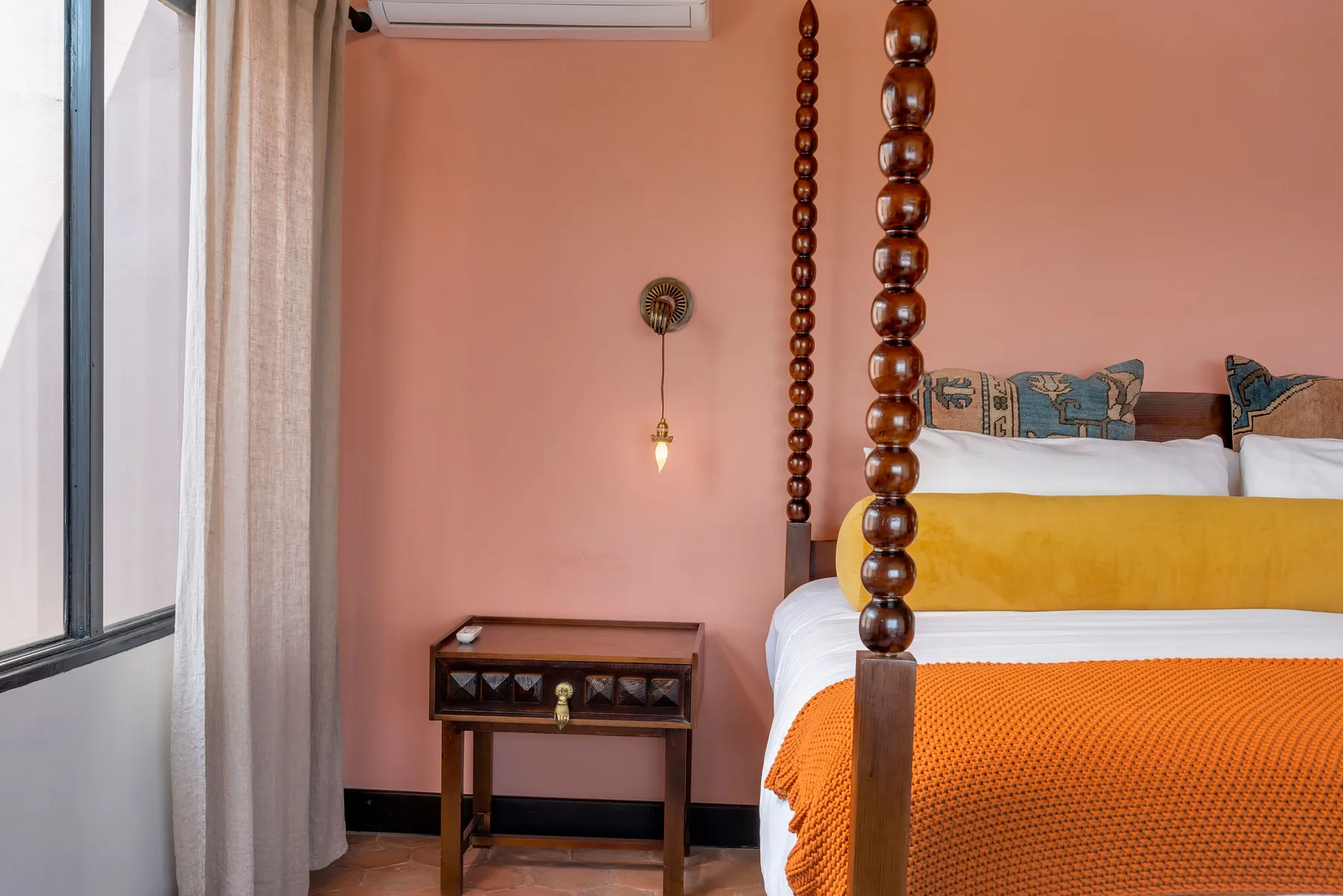 A bedroom with a bed dressed in white, yellow, and orange bedding.