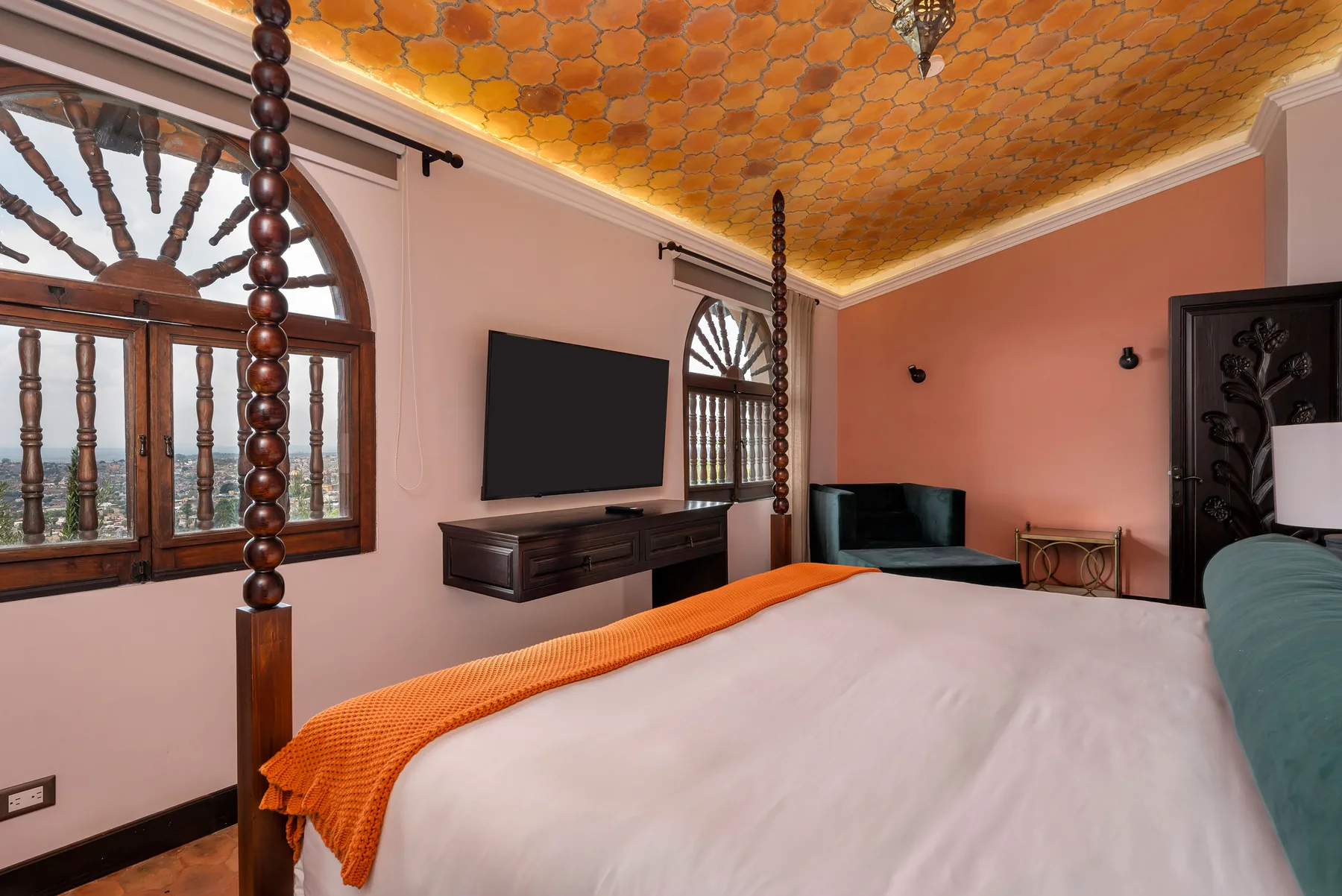 A bedroom with a large bed, wall-mounted television, and arched windows.