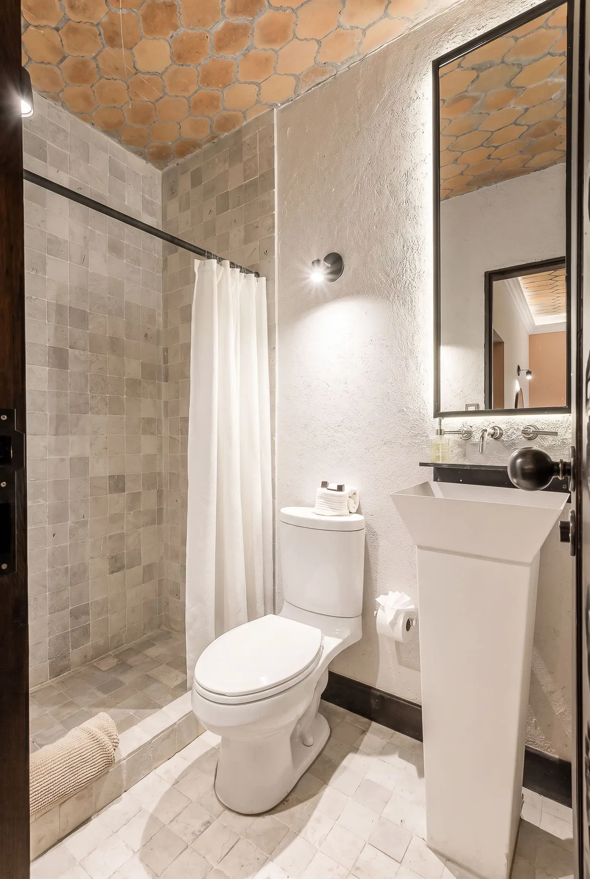 A bathroom with a tiled shower, toilet, and pedestal sink.