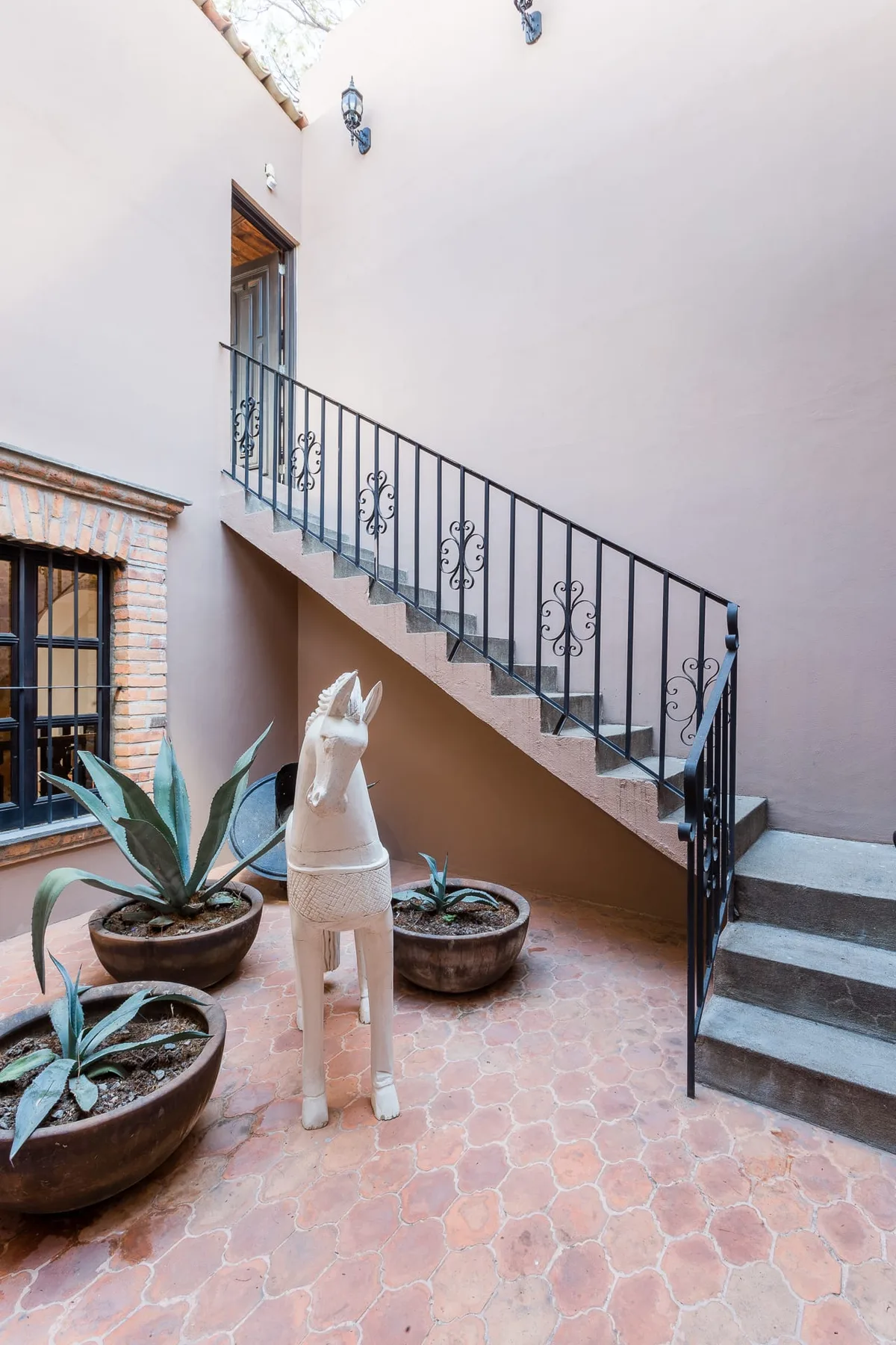 An outdoor stairway with a black metal railing overlooks a tiled courtyard with potted plants.