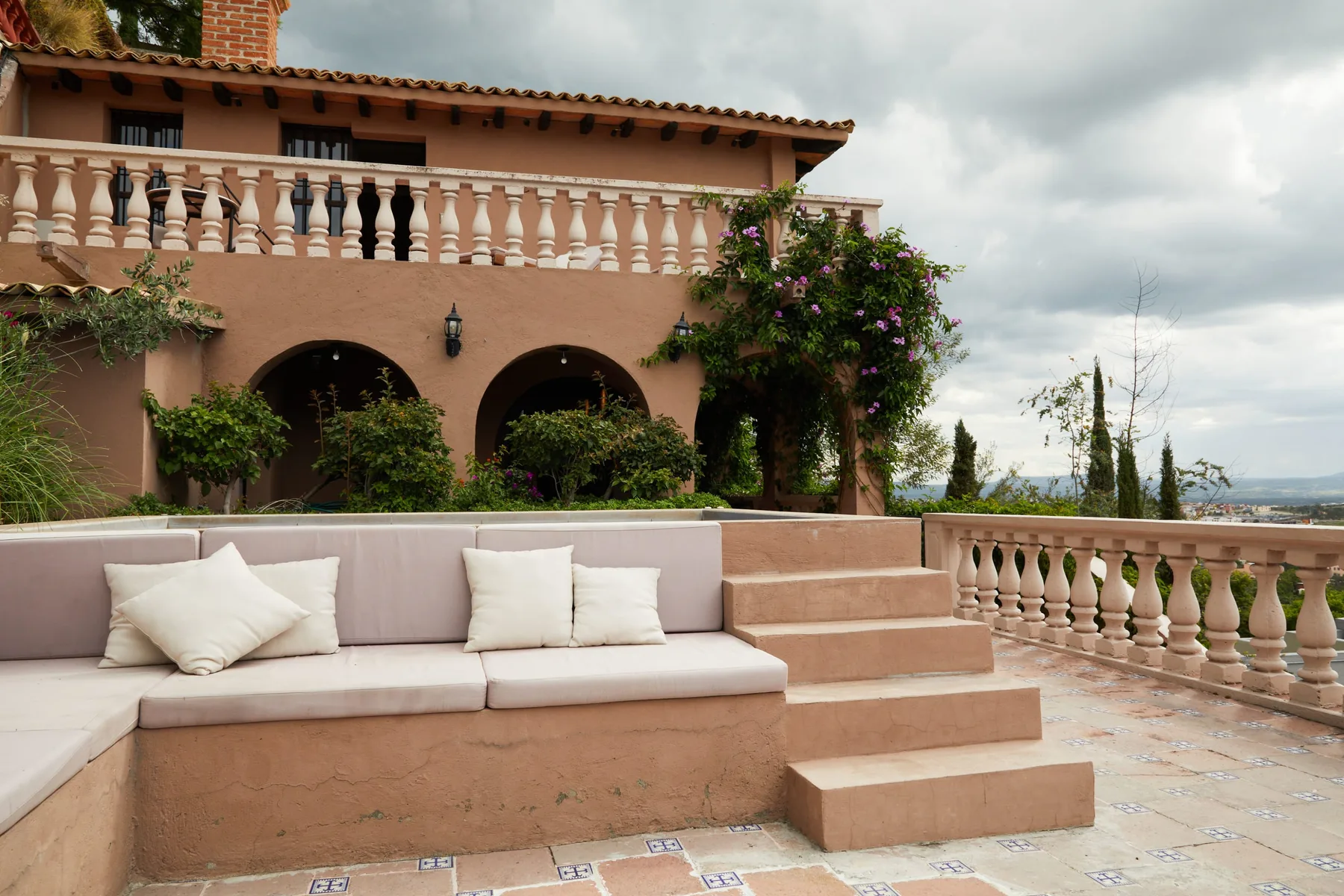 A tiled terrace has built-in seating beside a peach-colored building.