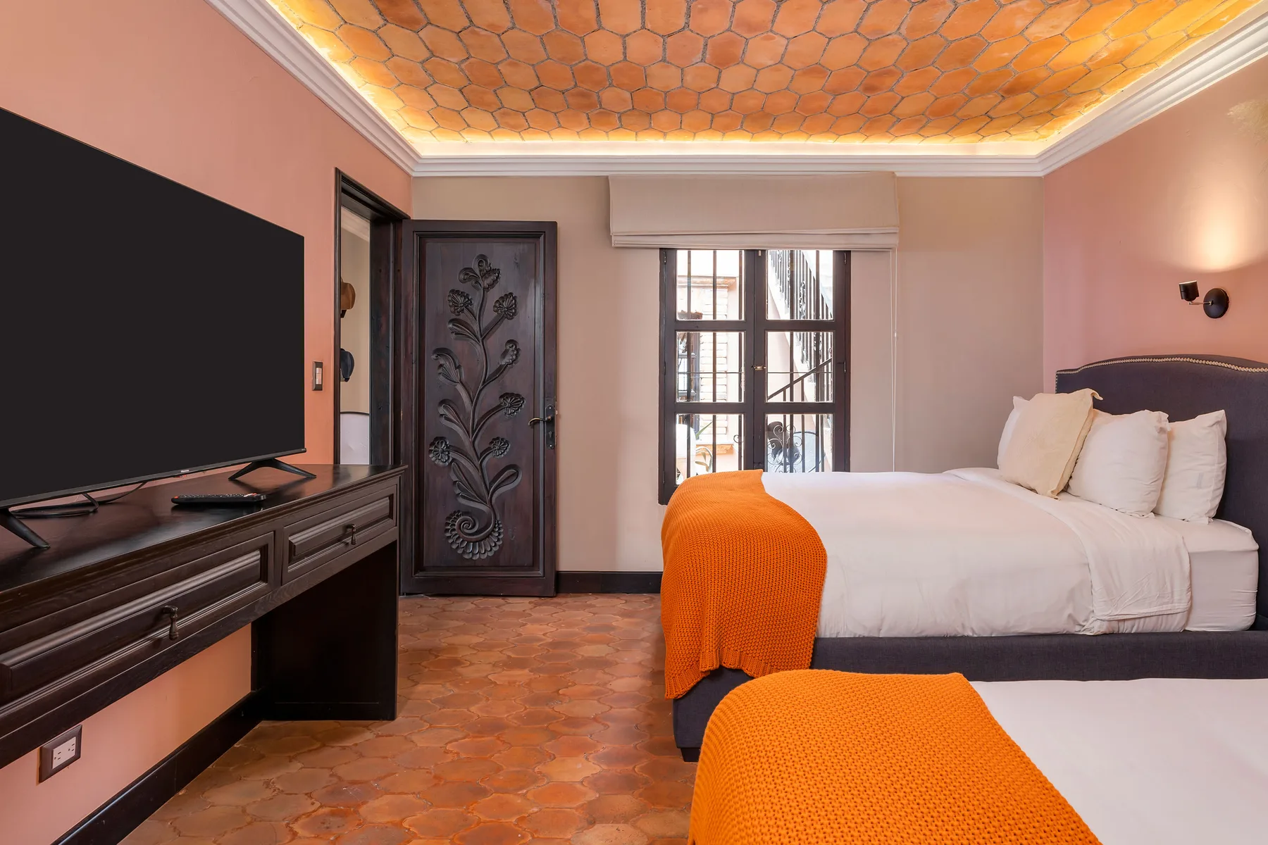 A bedroom with white bedding, orange bed throws, and a television on a cabinet.