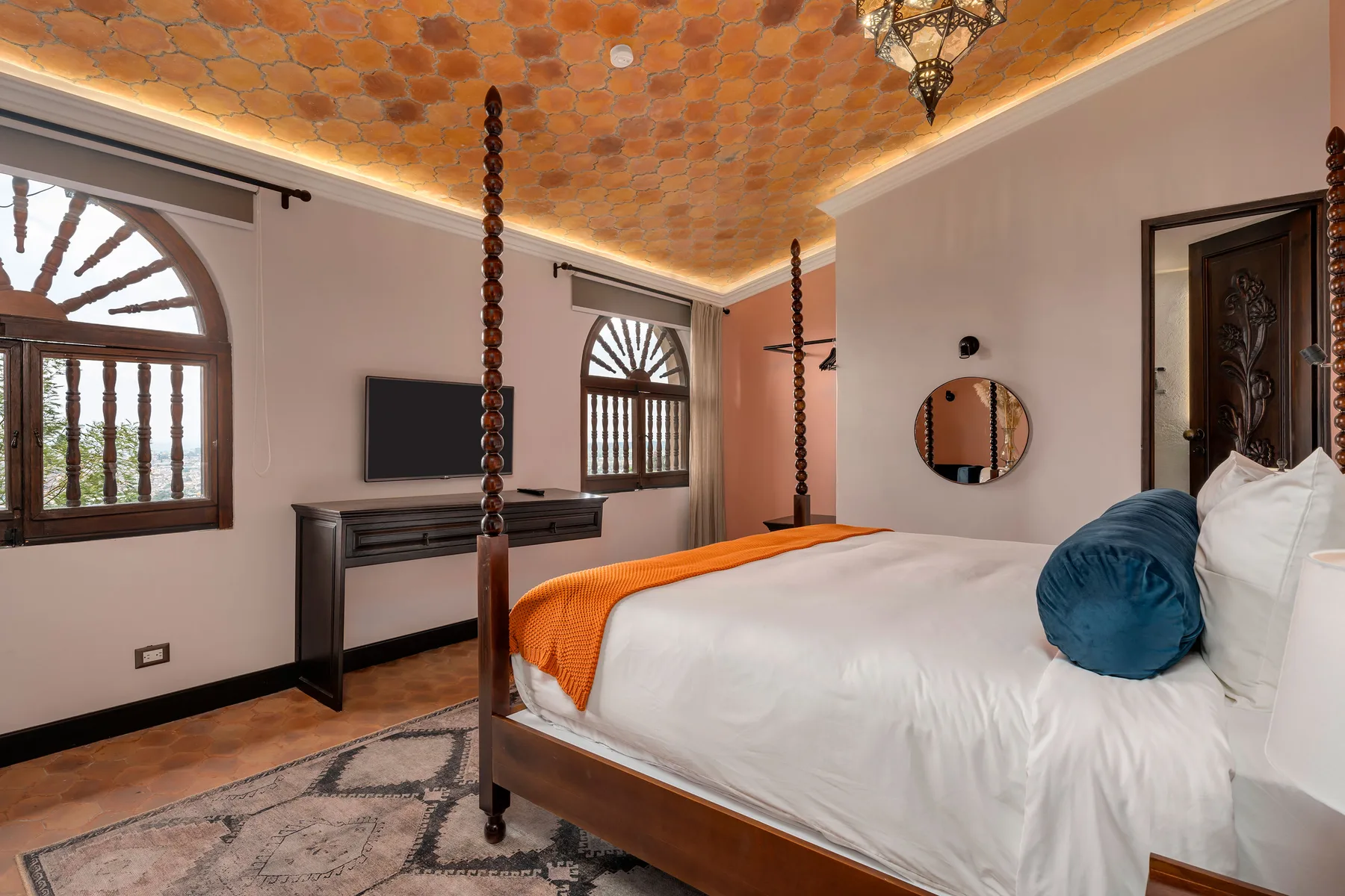 A bedroom with a white bed, orange throw, and arched windows.
