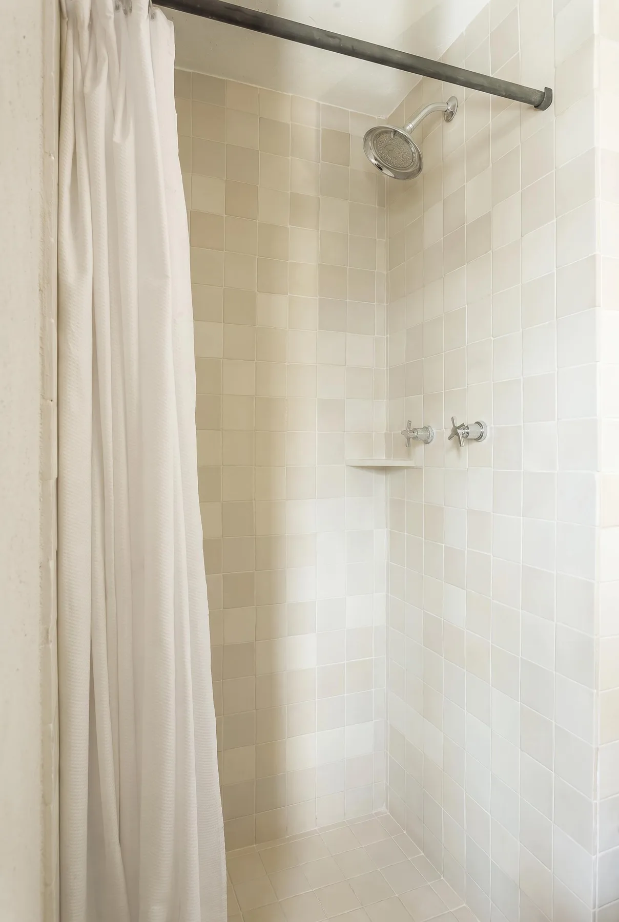 A tiled shower with a white curtain and wall-mounted showerhead.