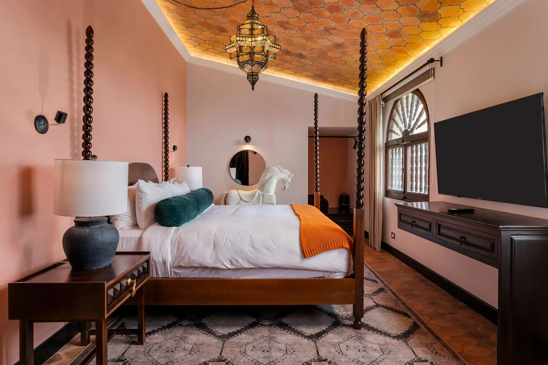 A bedroom with a large bed, a wall-mounted television, and a patterned ceiling.