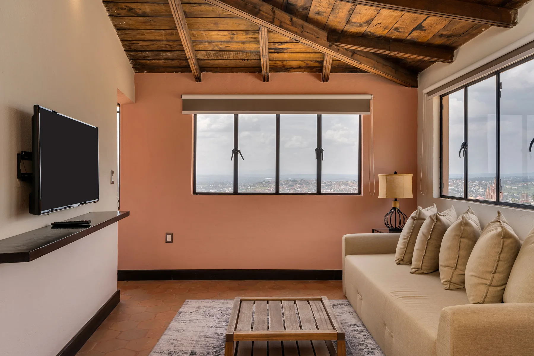 A living room with a beige sofa and large windows overlooking the city.