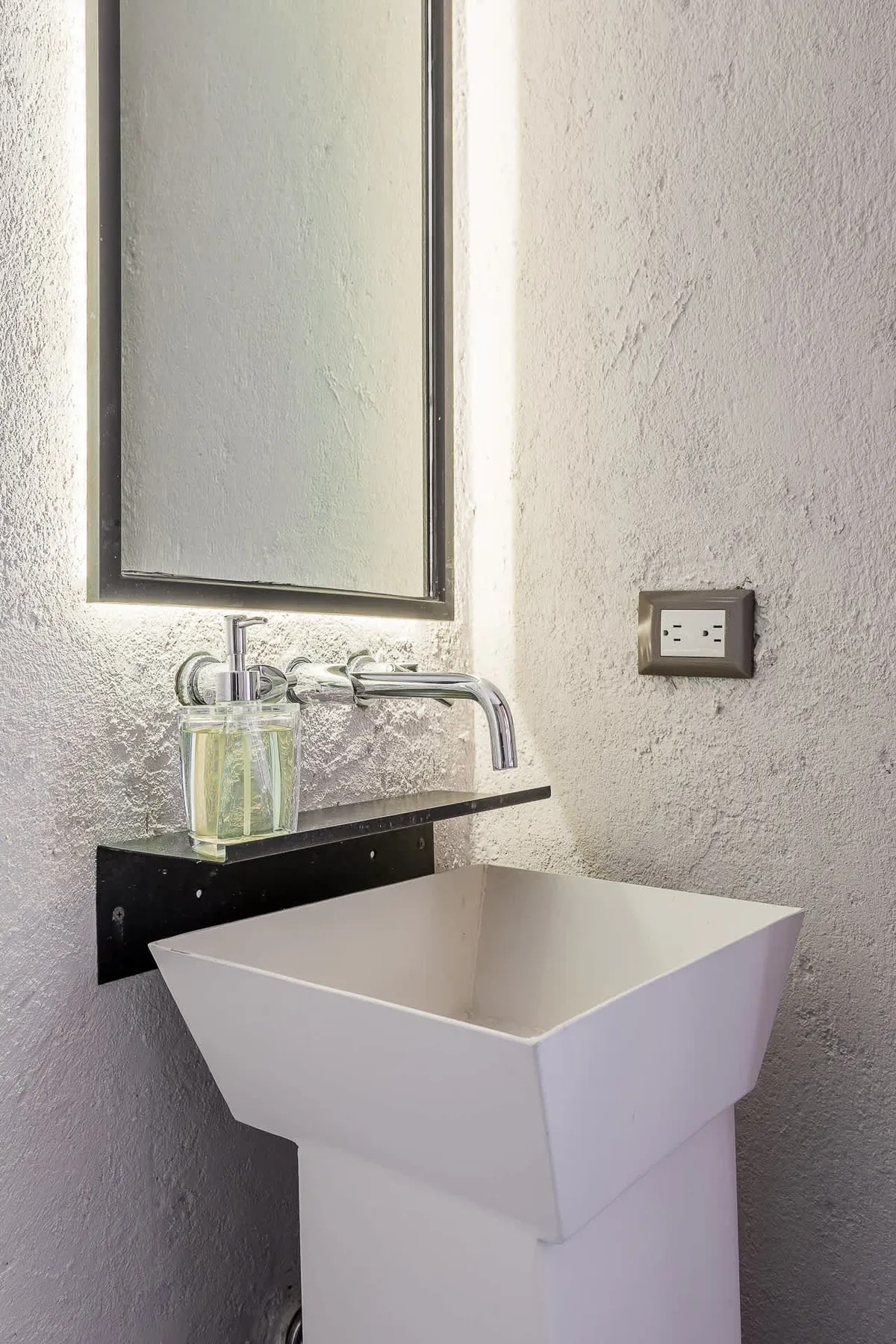 A bathroom sink with a wall-mounted faucet and mirror.