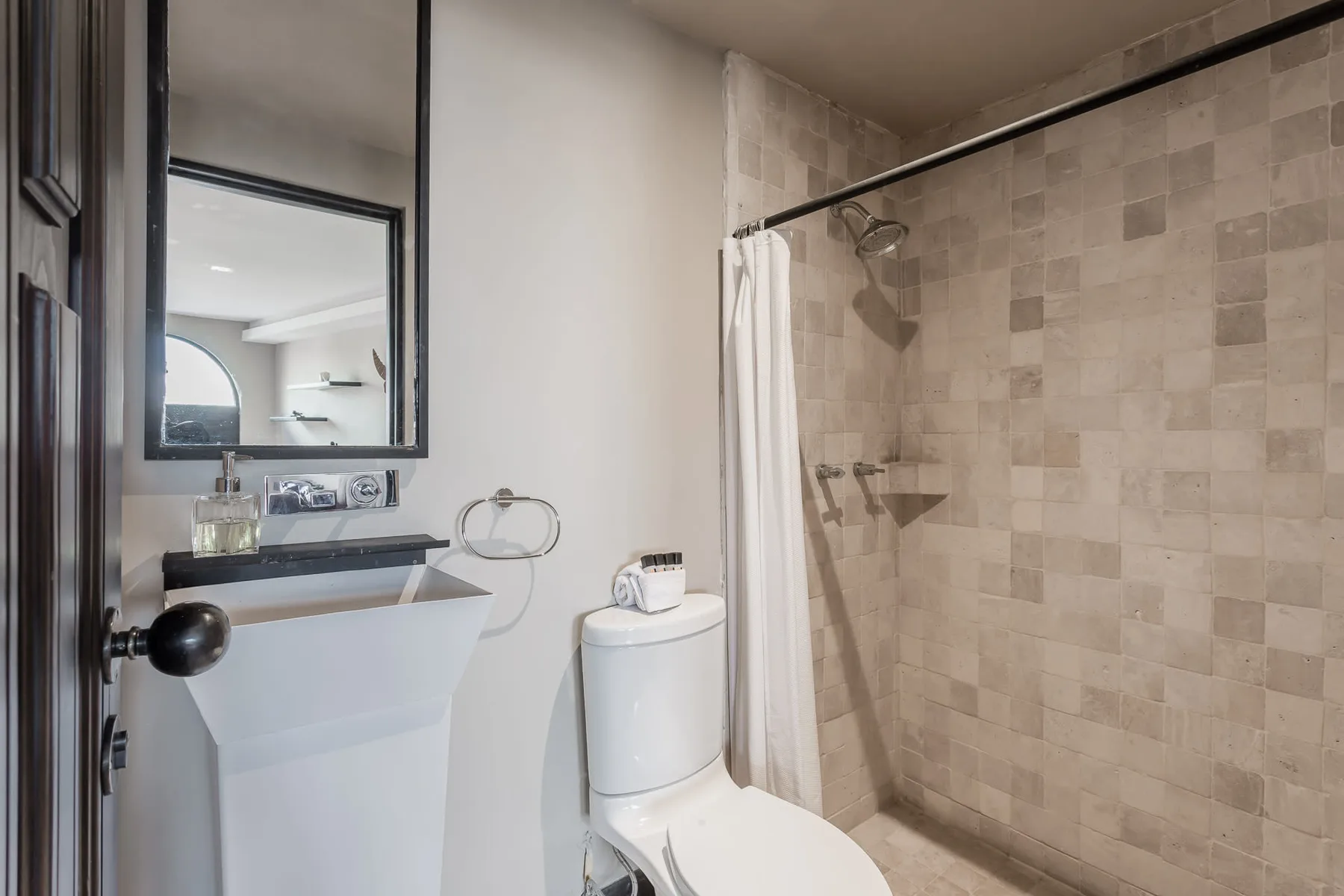 A bathroom with a sink, mirror, toilet, and tiled shower area.