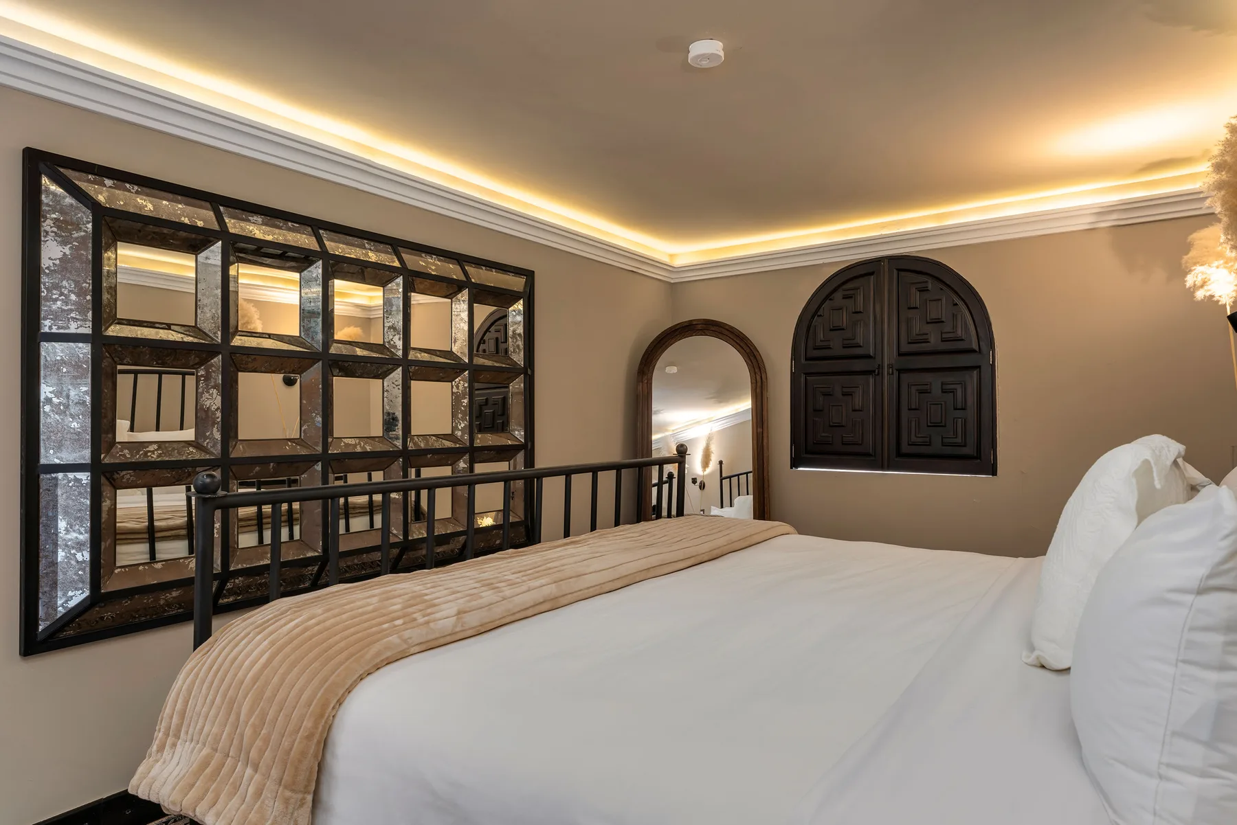 A bedroom with a large bed, decorative mirror panels, and warm ceiling lighting.