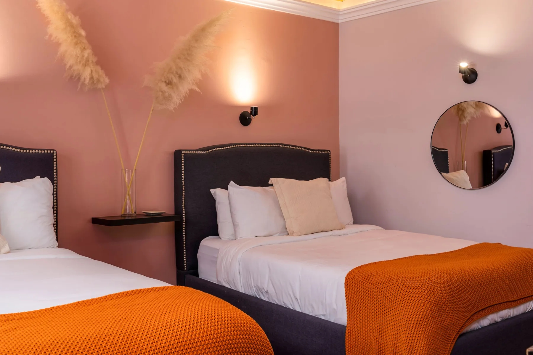 A bedroom with two beds dressed in white bedding and orange throws.