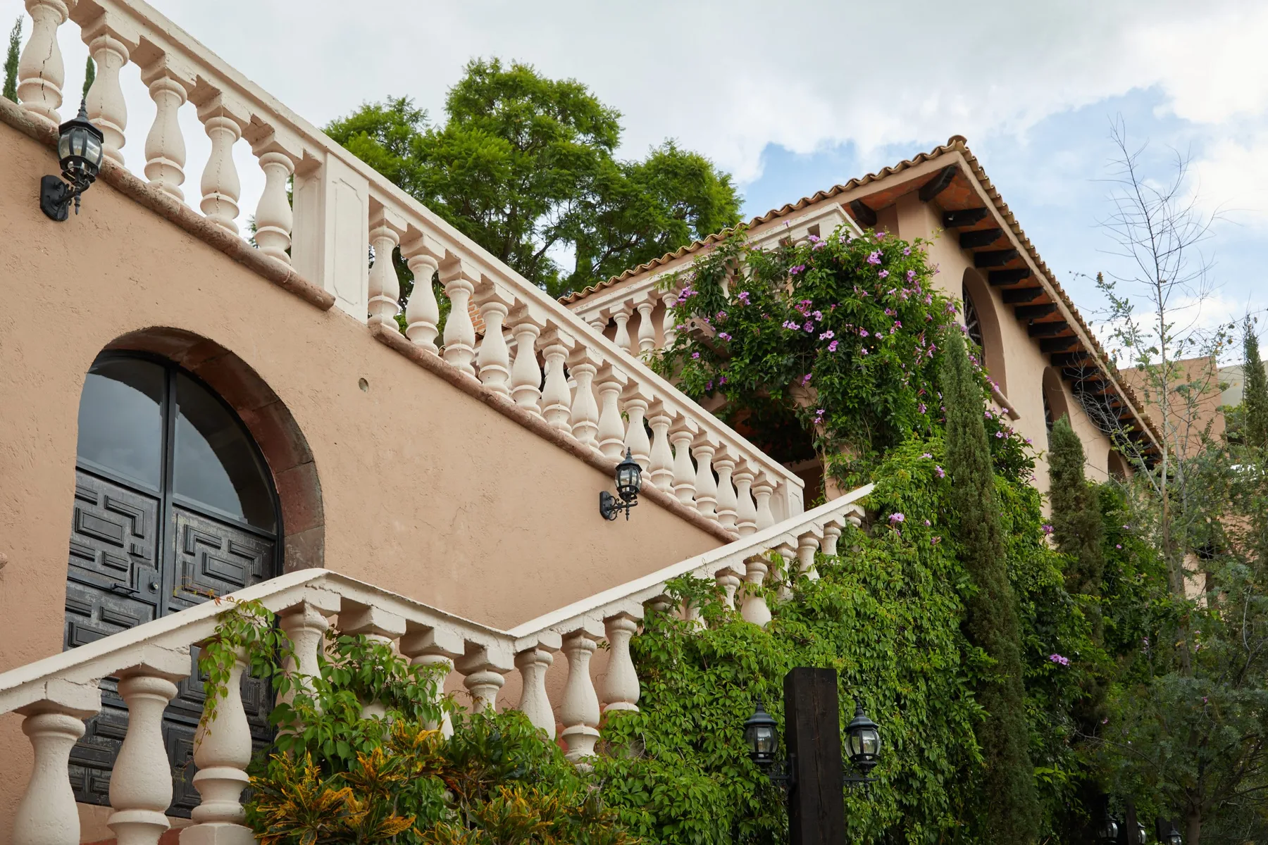 A stucco building exterior with ornate railings and climbing greenery.