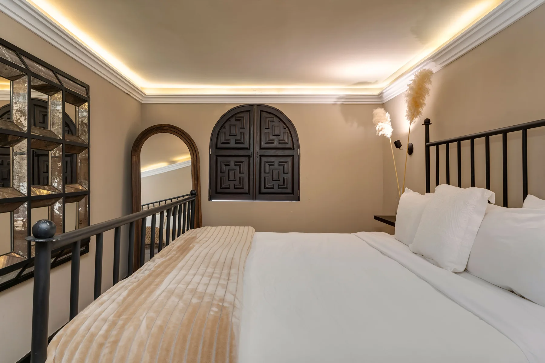 A bedroom with a white bed, black metal headboard, and arched windows.