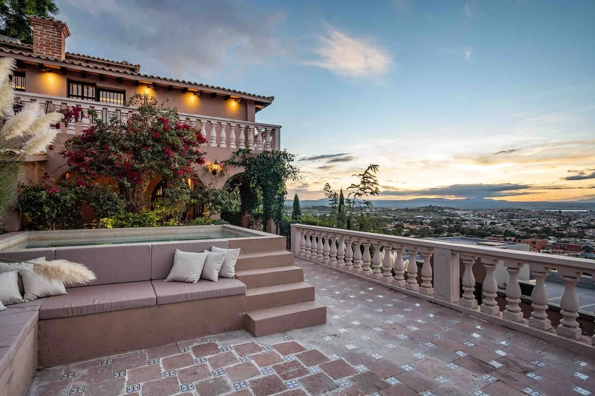 A tiled terrace with cushioned seating overlooks a town beneath the evening sky.