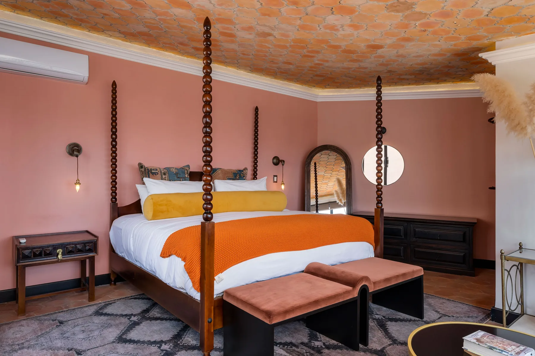 A bedroom with a four-poster bed, orange bedding, and a cushioned bench.