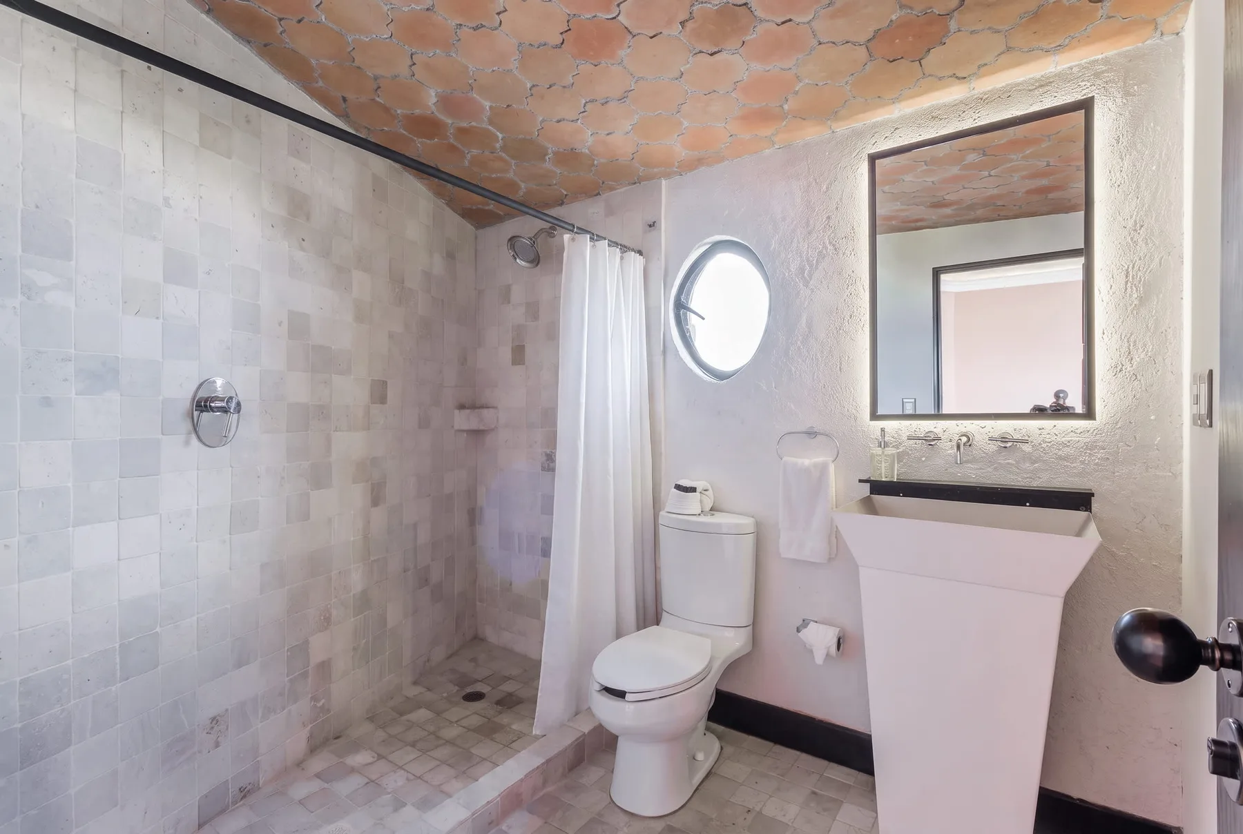A tiled bathroom with a toilet, sink, and round window.