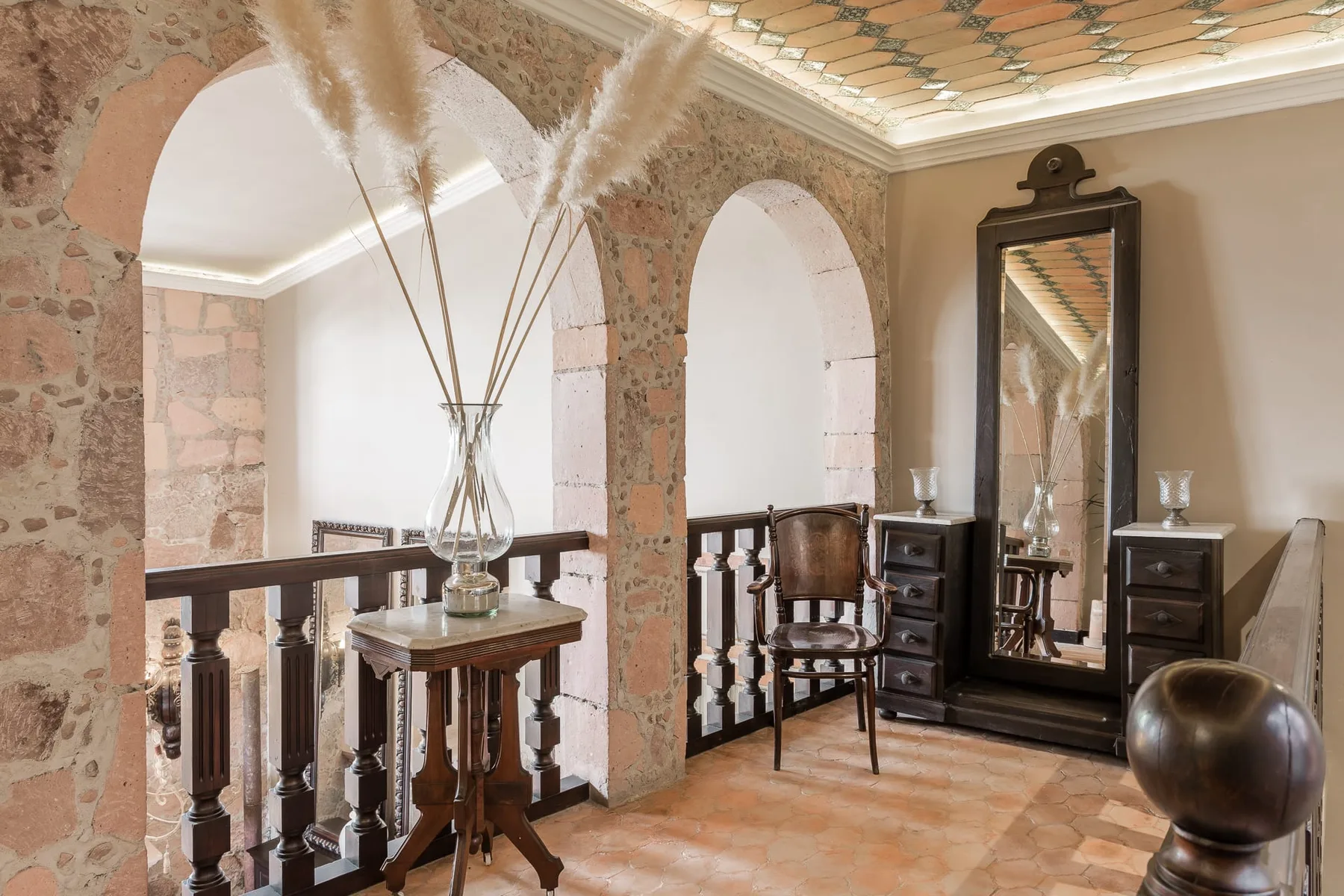 A furnished room with stone arches, a wooden railing, and a tall mirror.
