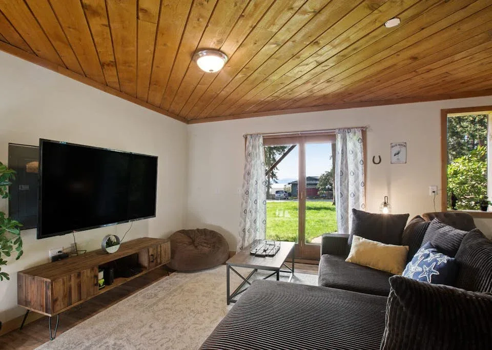 A living room with seating, a television, and glass doors opening onto a green yard.