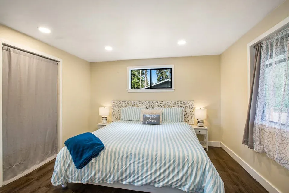 A bright bedroom with a neatly made bed and windows on two walls.