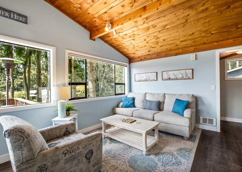 A bright living room with seating, a coffee table, and large windows.