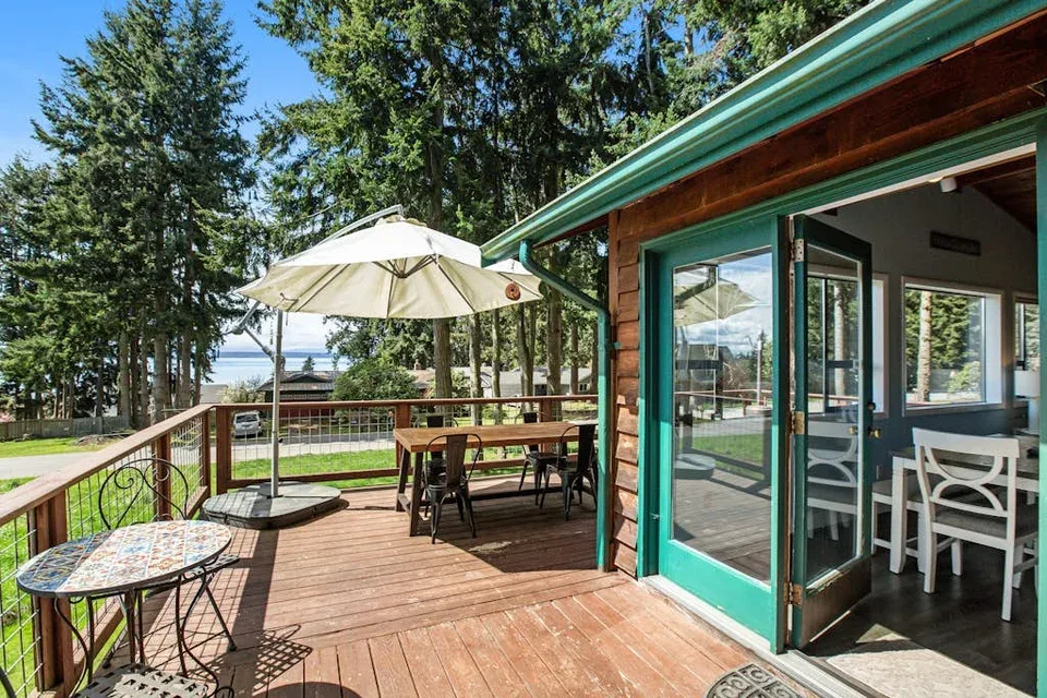 A wooden deck with an open doorway and outdoor seating overlooks a green yard.