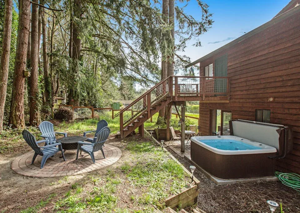 An outdoor seating area and hot tub beside a wooded house.