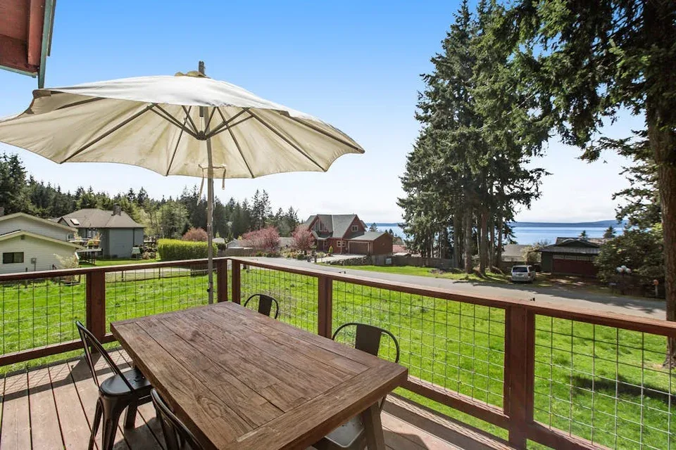 A wooden deck overlooks a grassy yard, nearby houses, and a glimpse of water.