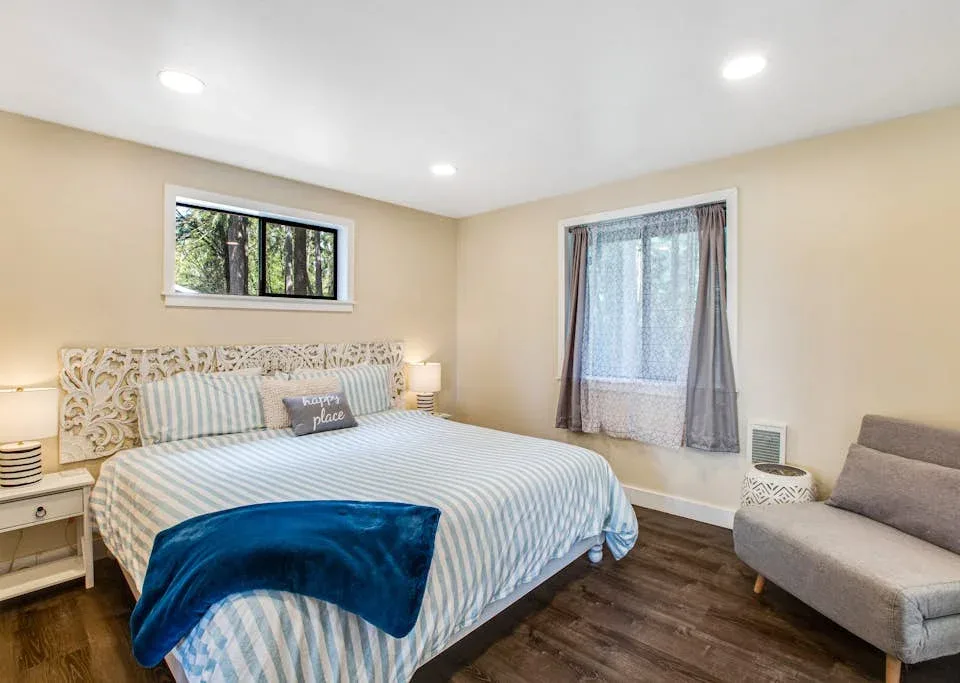A bedroom with a large bed, a curtained window, and a small seating area.