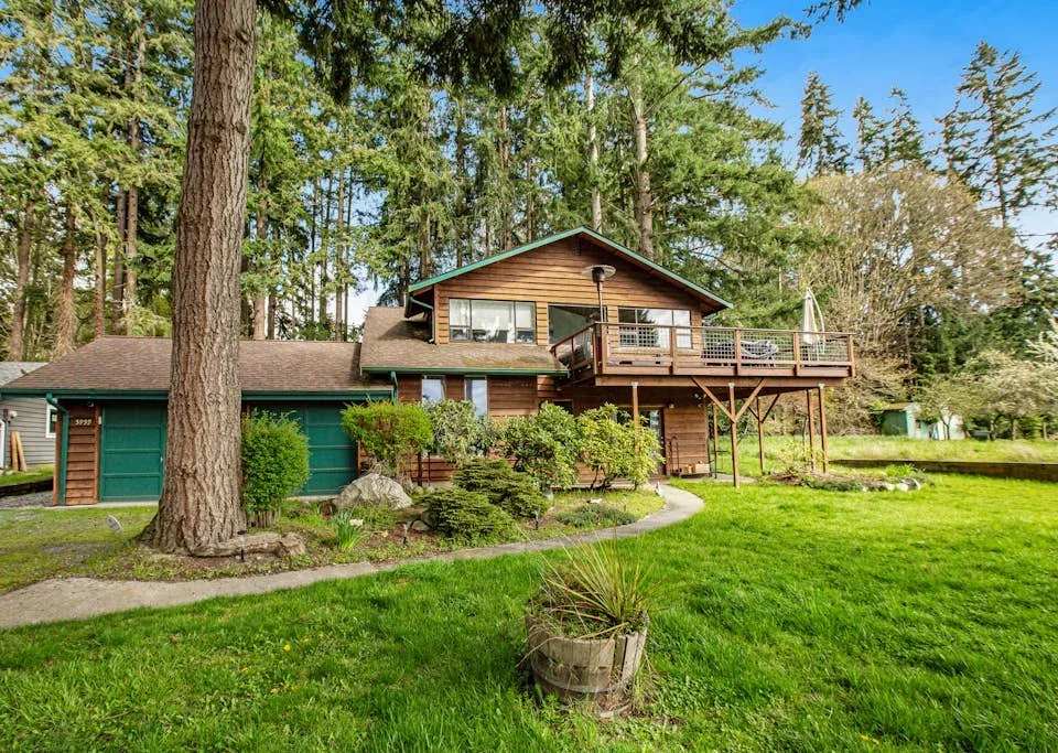 A wooded house with a raised deck overlooks a green lawn.