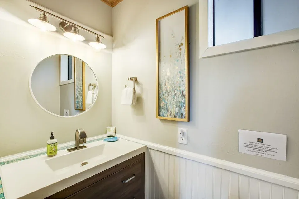A bathroom vanity with a sink, round mirror, and framed wall art.