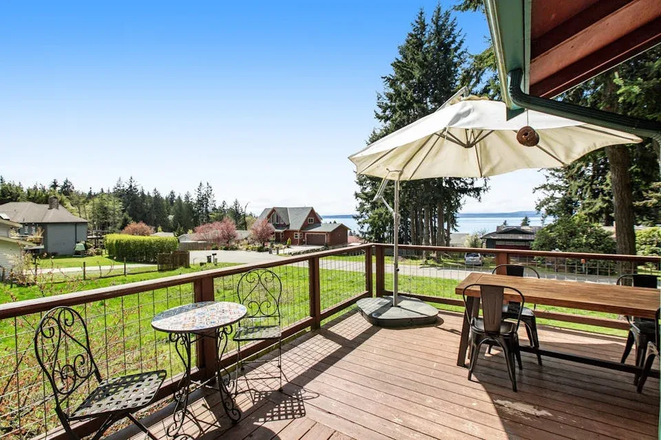 A wooden deck with outdoor seating and an umbrella overlooks a grassy yard.