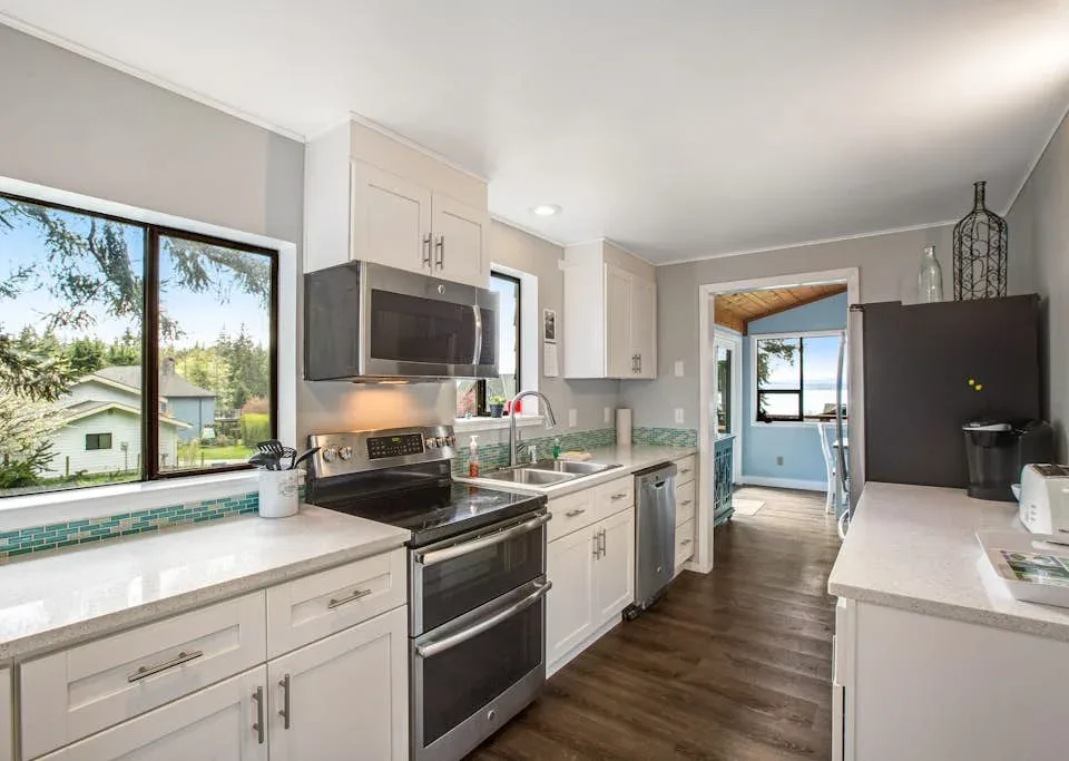 A bright kitchen with white cabinets, dark appliances, and a window overlooking greenery.