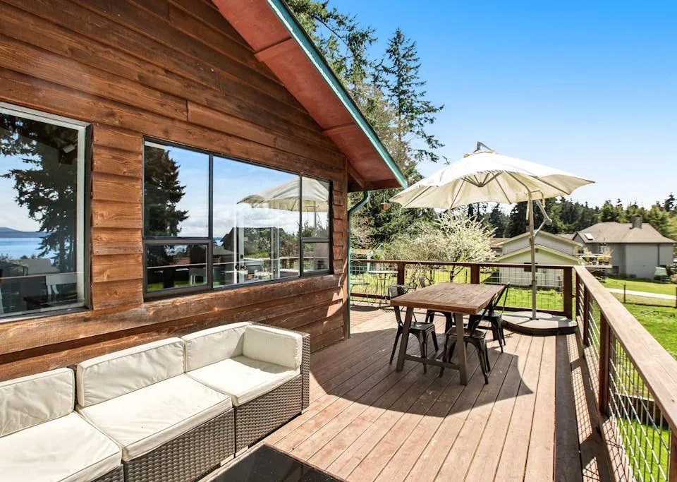 A wooden deck beside a house has outdoor seating and a patio umbrella.